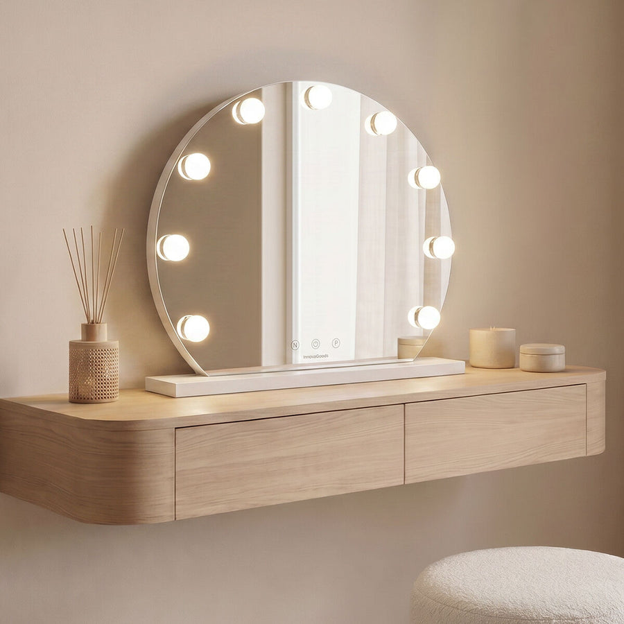 Round white LED vanity mirror with nine bulbs standing on a dressing console beside a reed diffuser